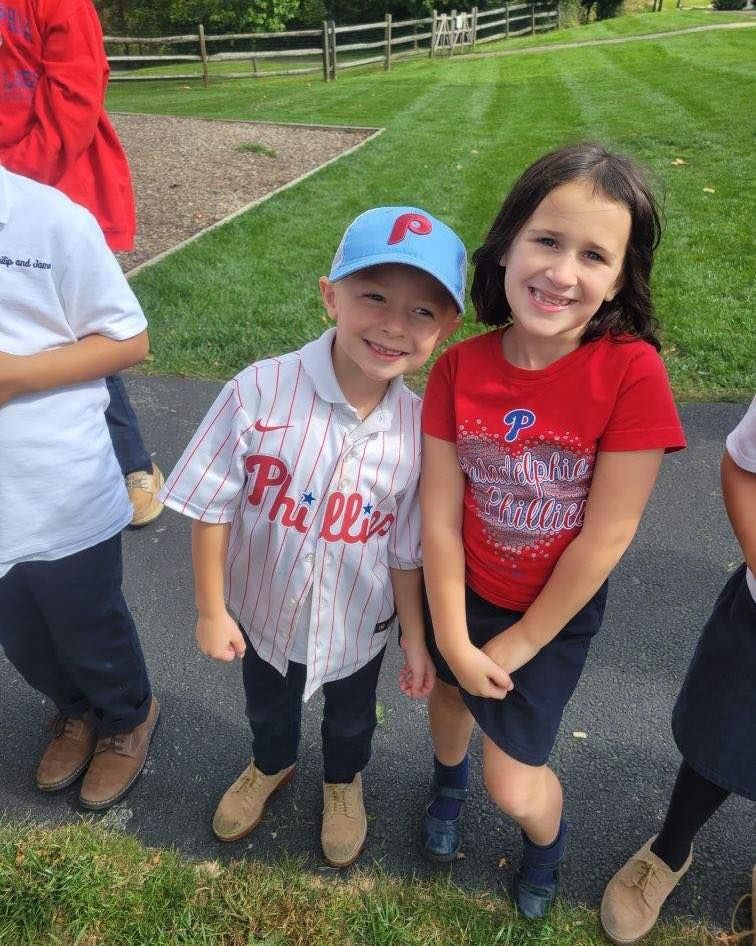A boy in a phillies jersey stands next to a girl in a red shirt