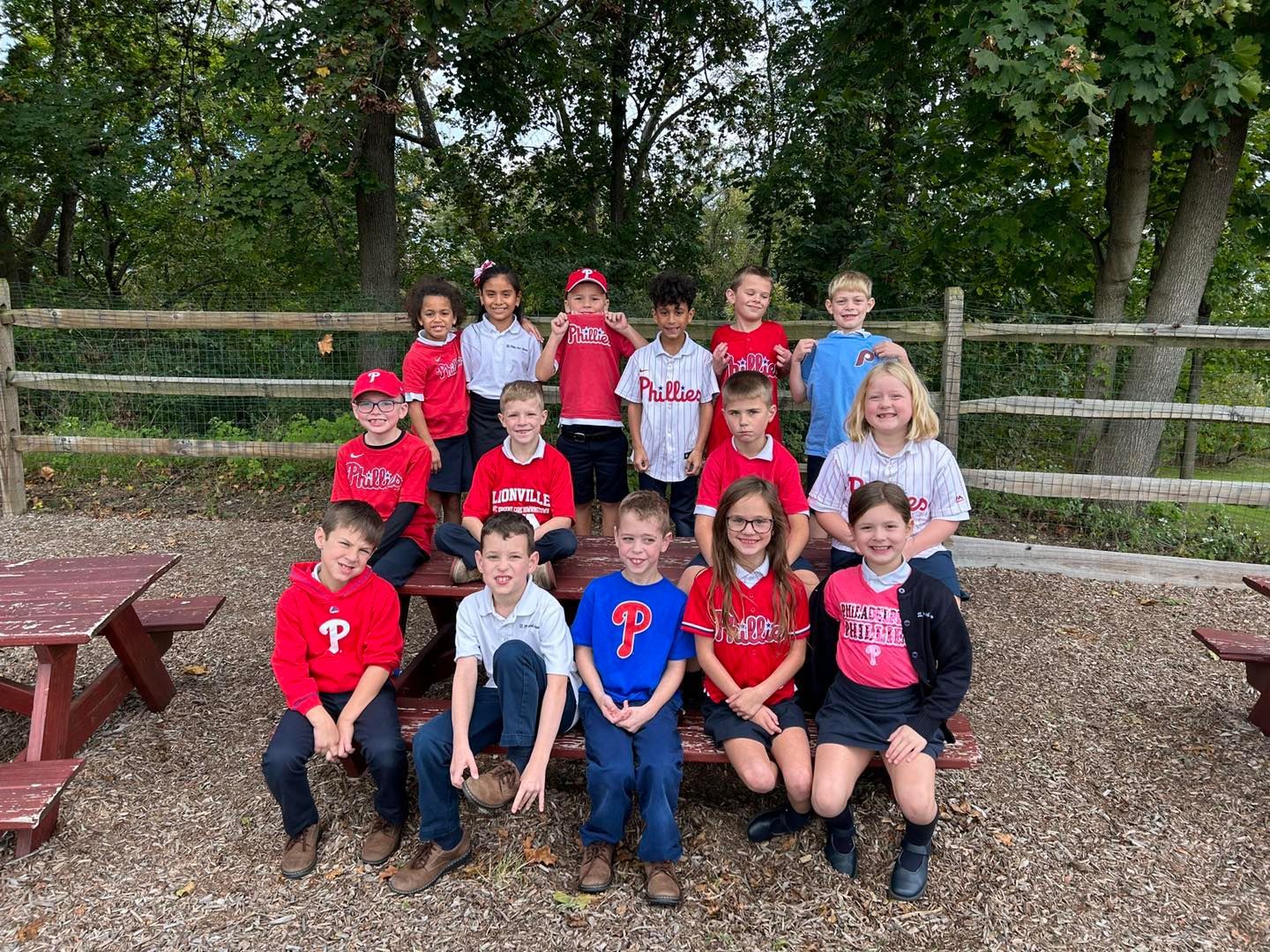 A group of children are sitting on picnic tables in a park.