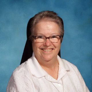 A woman wearing glasses and a white shirt is smiling in front of a blue background.