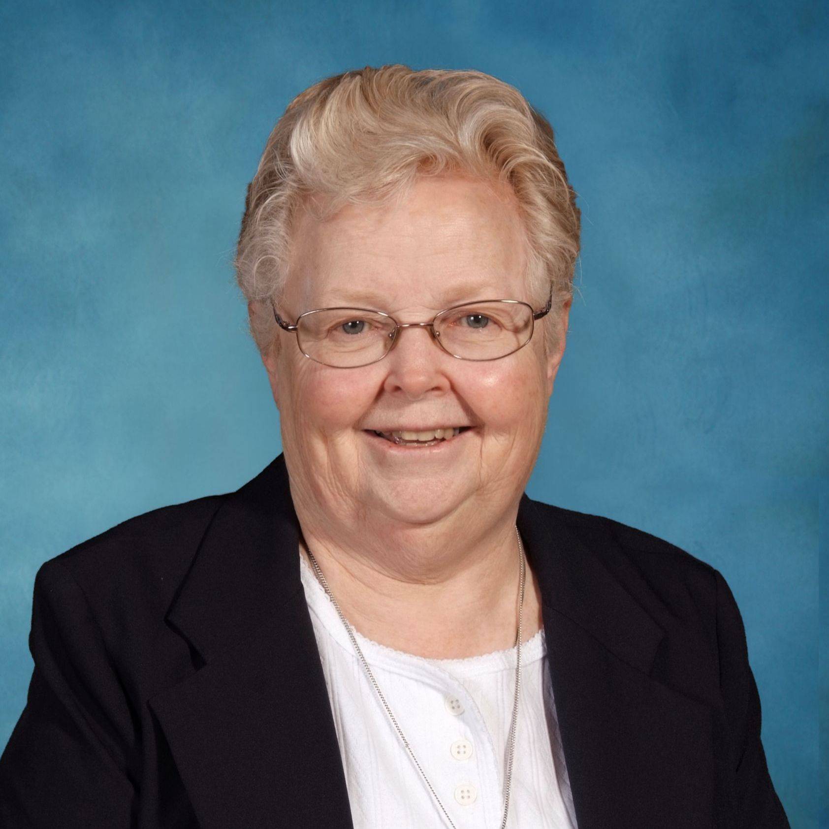 A woman wearing glasses and a black jacket is smiling for the camera
