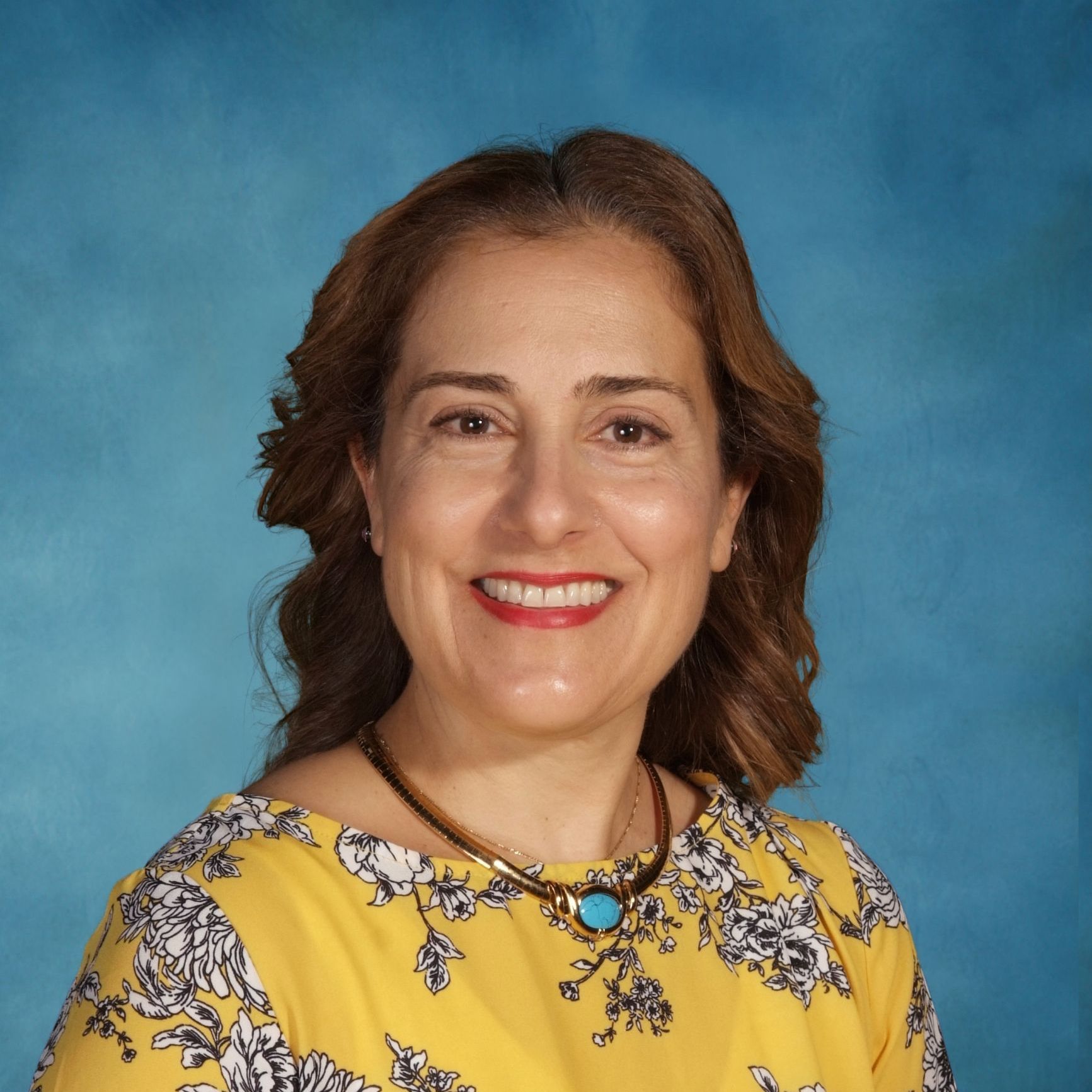 A woman wearing a yellow shirt and a turquoise necklace is smiling for the camera.