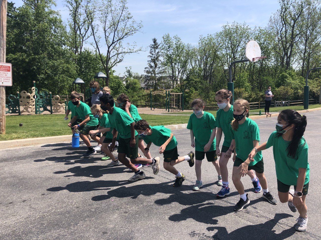 A group of children in green shirts are running down a street.