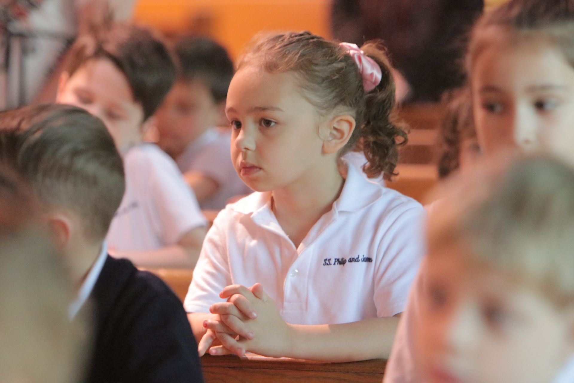 A little girl is sitting in a classroom with other children.