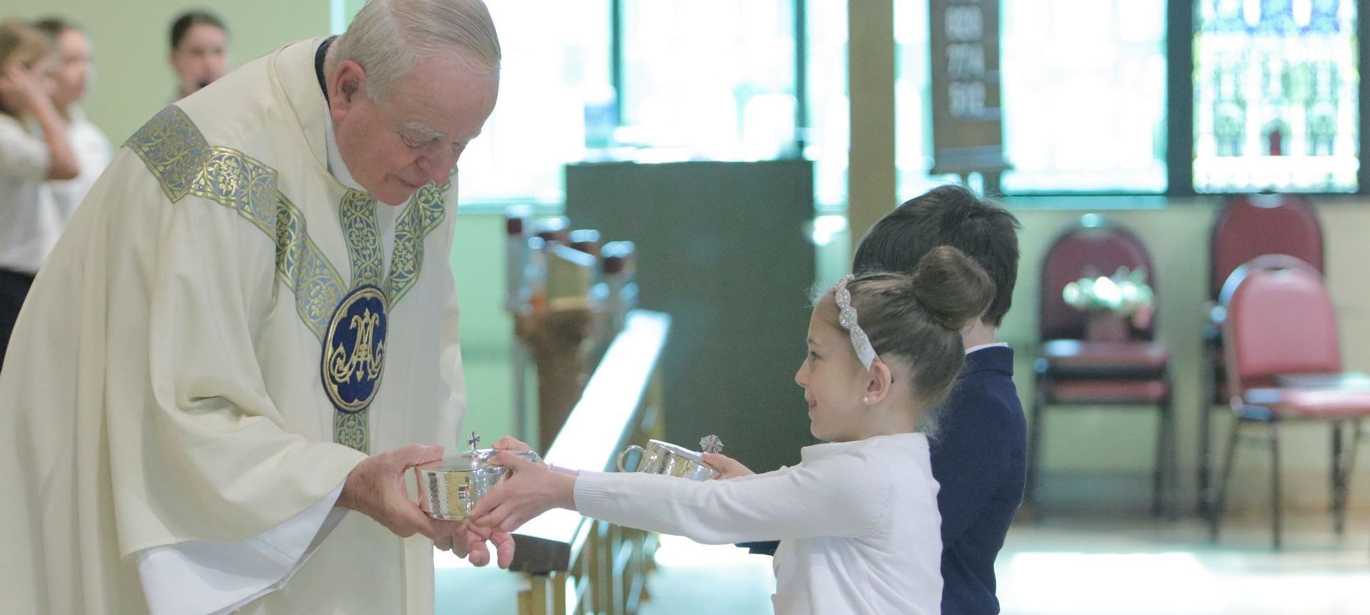 Two young children presenting a priest with gifts in church.