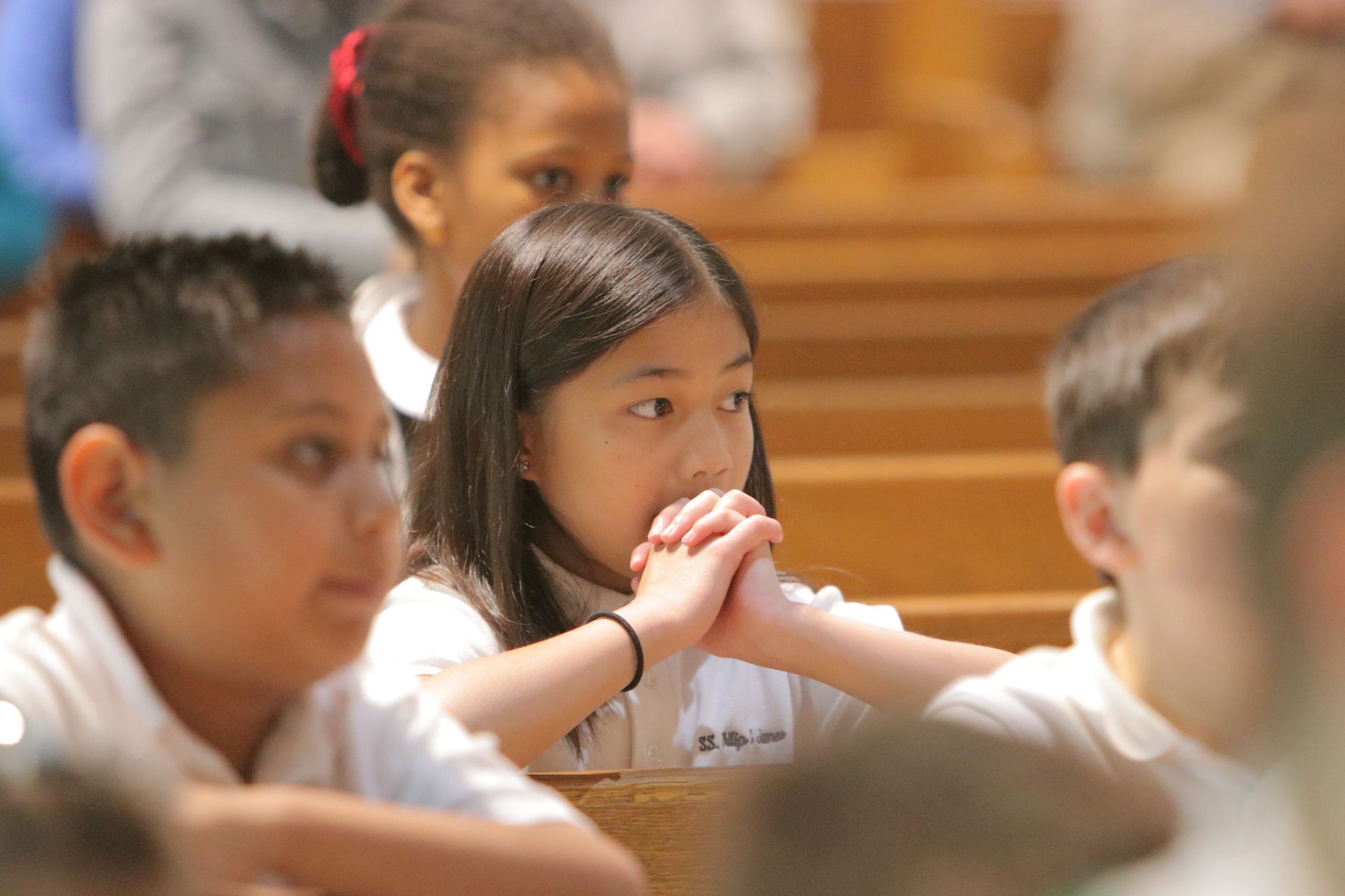 A group of children are sitting in a church with their hands folded in prayer.