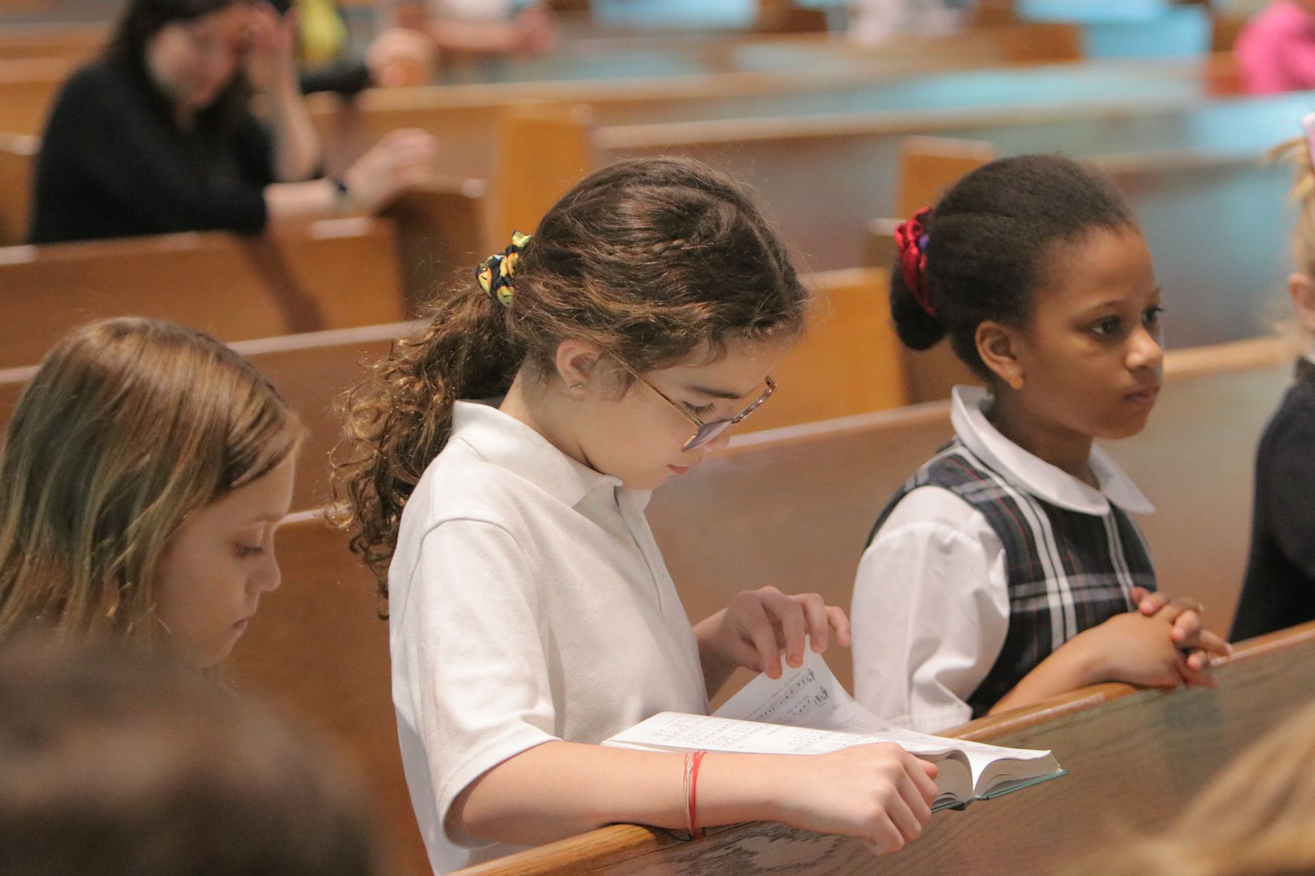 A group of young girls are sitting in a church reading the bible.