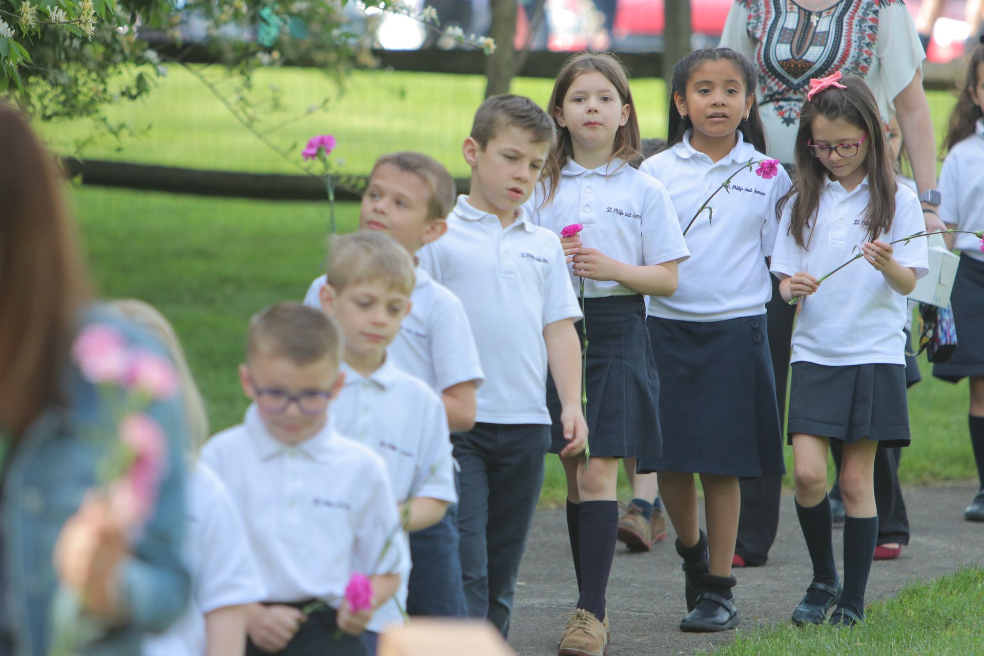 A group of children are walking down a path holding flowers.