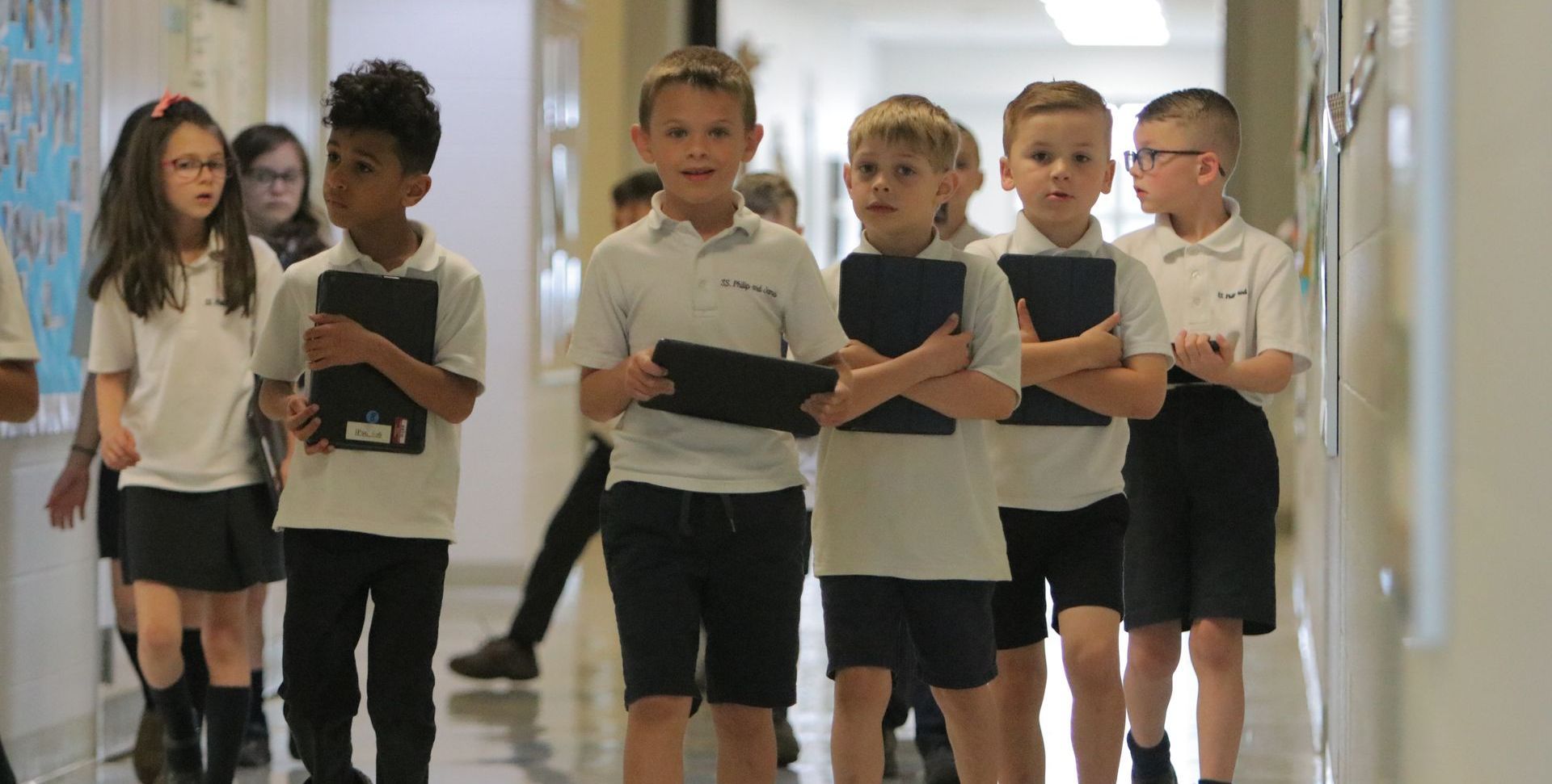 A group of children in school uniforms are walking down a hallway.