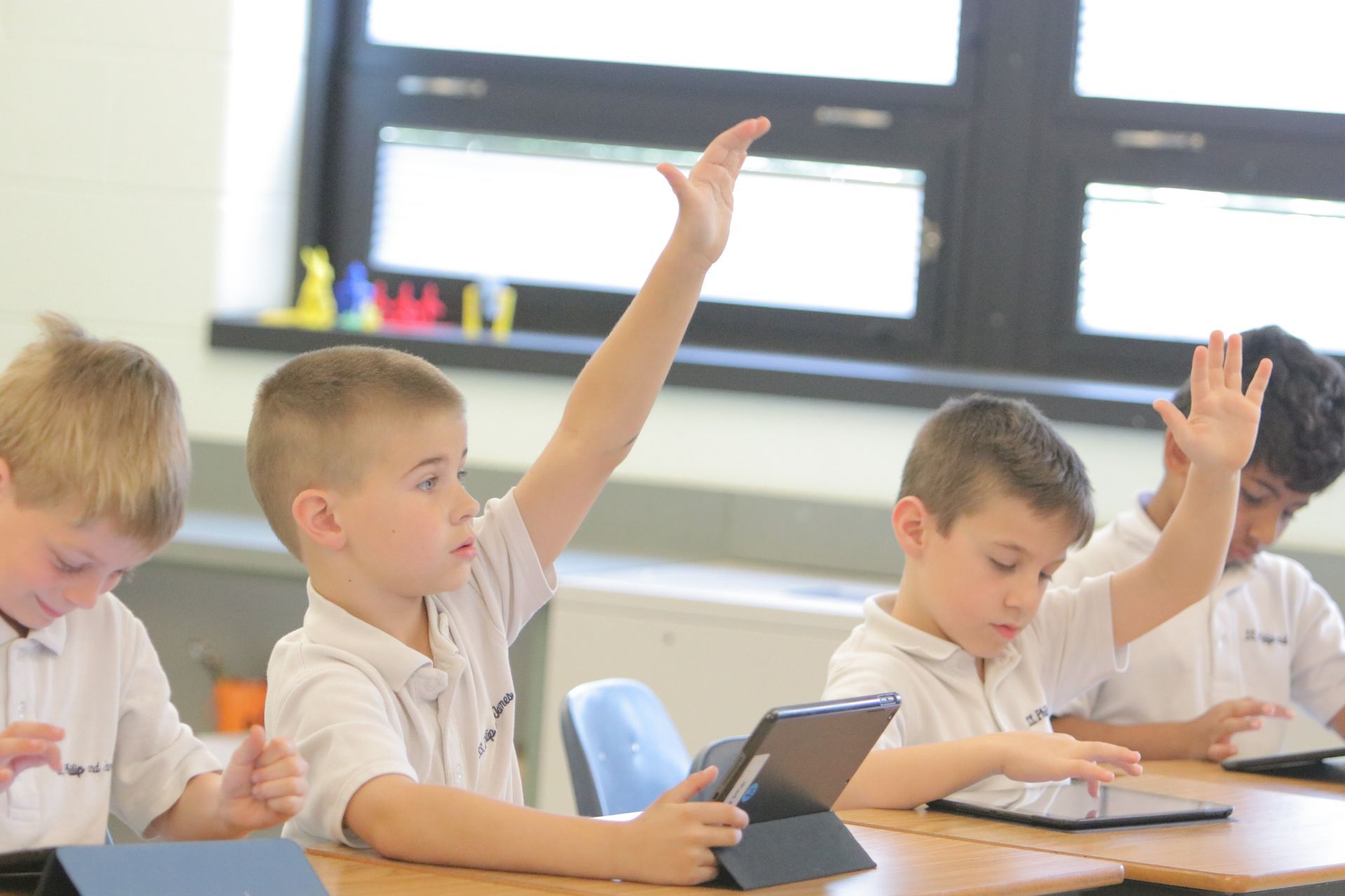 A group of young boys are raising their hands in a classroom.