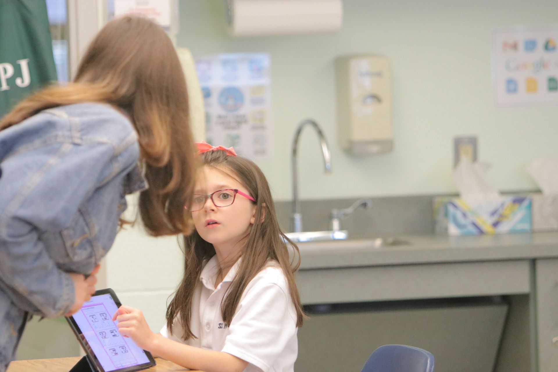 Two girls are looking at a tablet in a classroom.