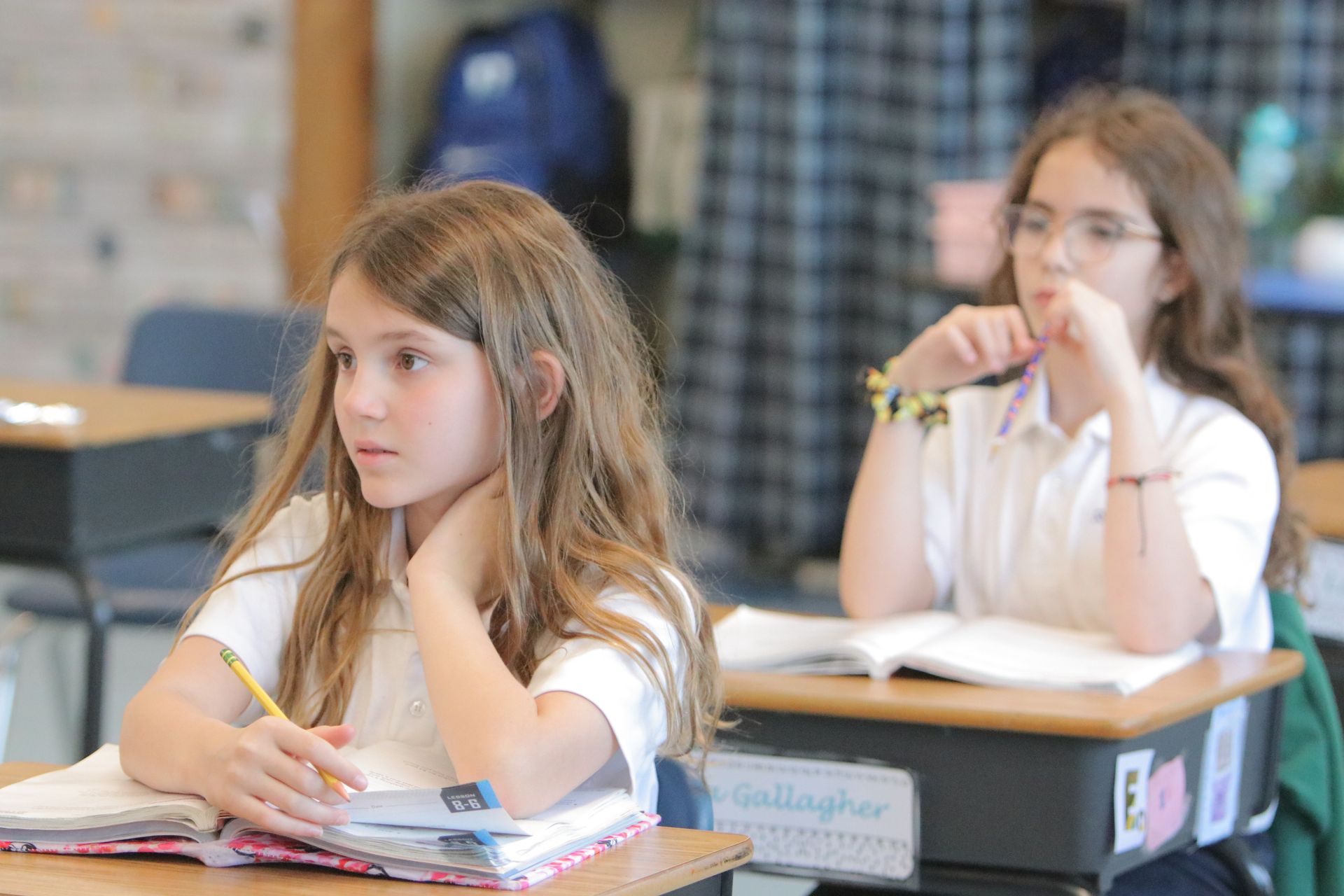 Two young girls are sitting at desks in a classroom.