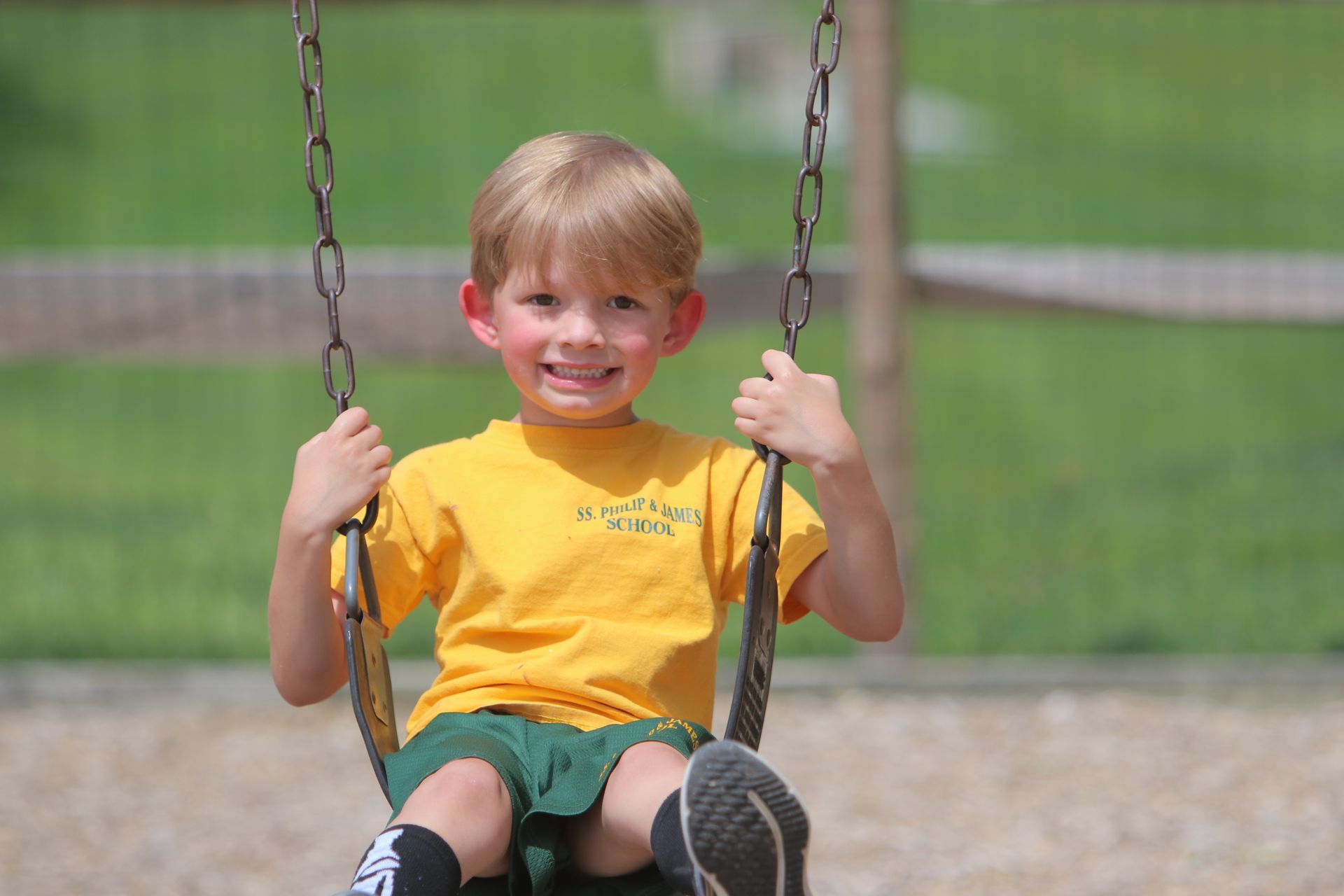 A young boy in a yellow shirt is sitting on a swing