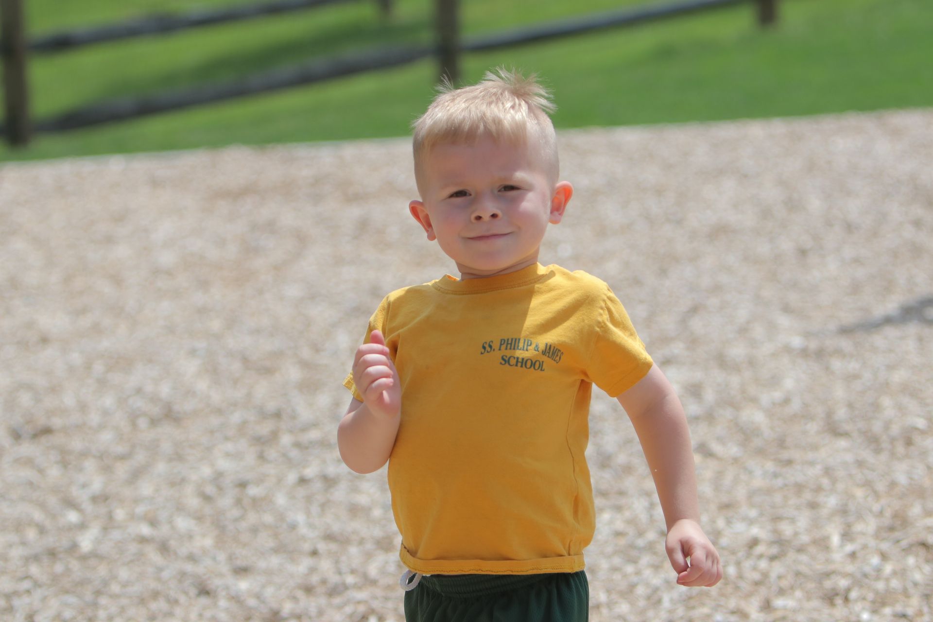 A young boy in a yellow shirt is running on a gravel path.
