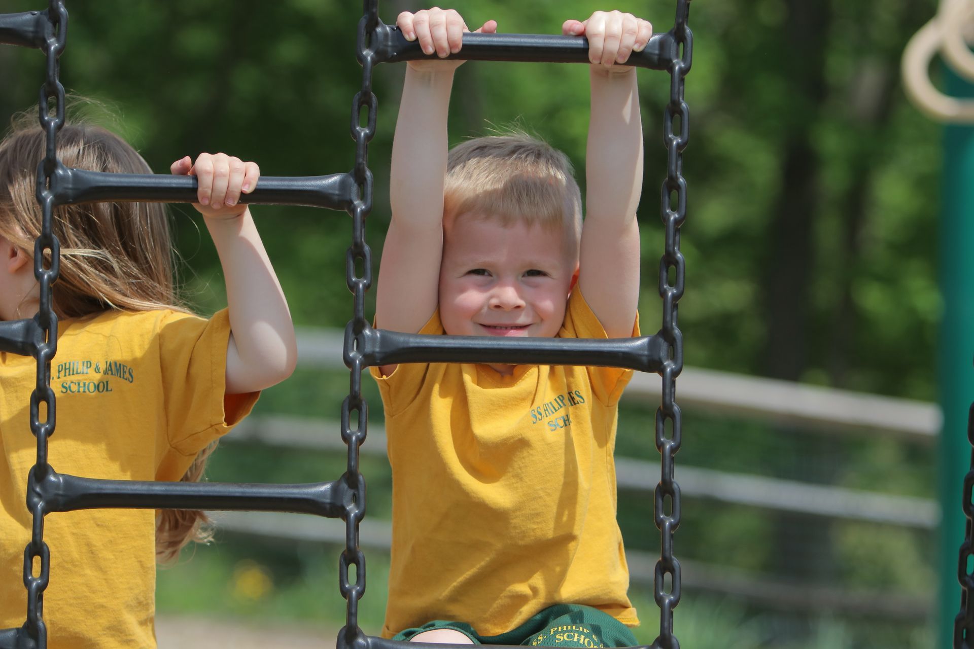 A boy and a girl are playing on a ladder at a playground.