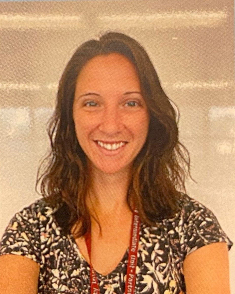 A woman wearing a lanyard around her neck is smiling for the camera.
