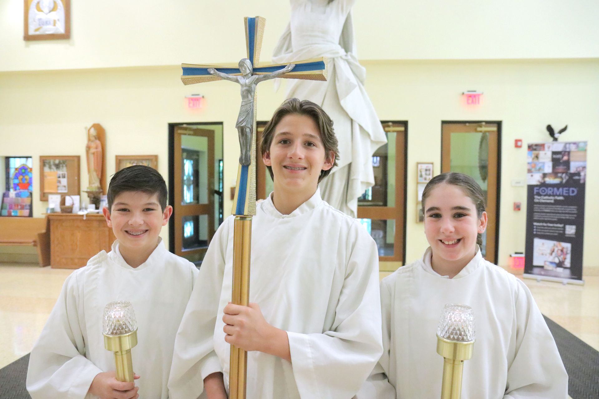 A boy and two girls are holding a cross in a church.