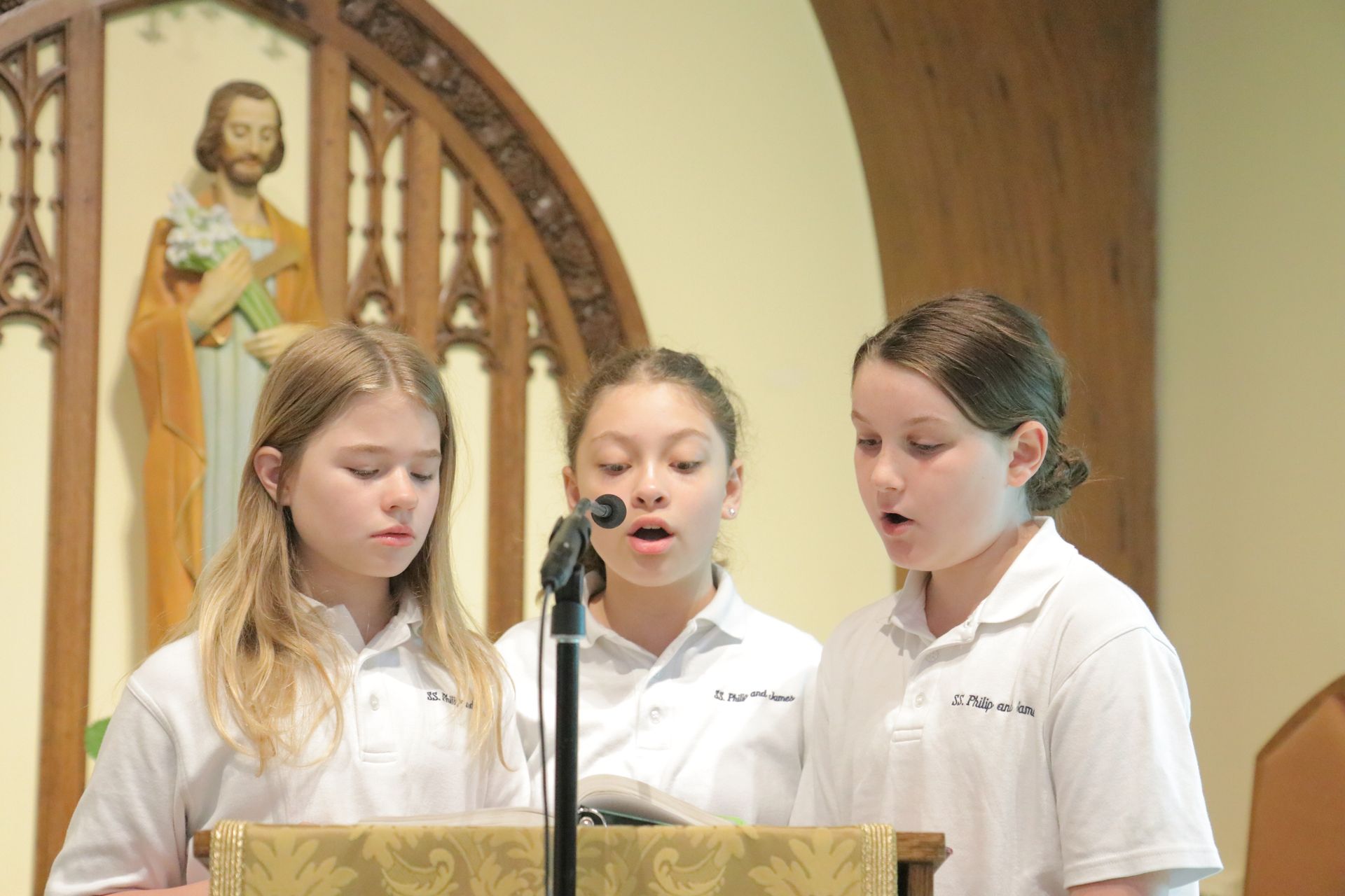 Three young girls are singing in front of a microphone in a church.