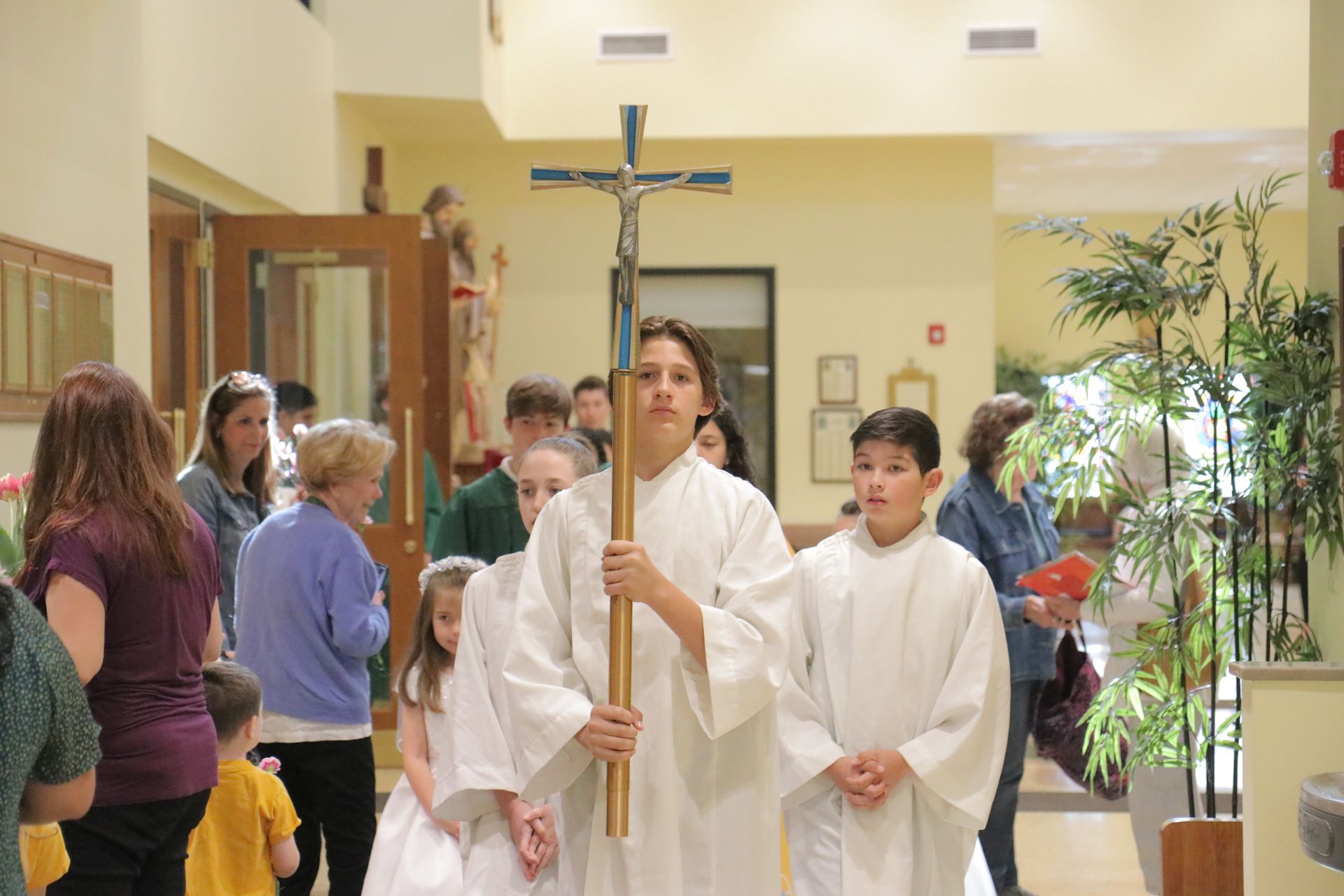 A group of people are walking down a hallway holding a cross.