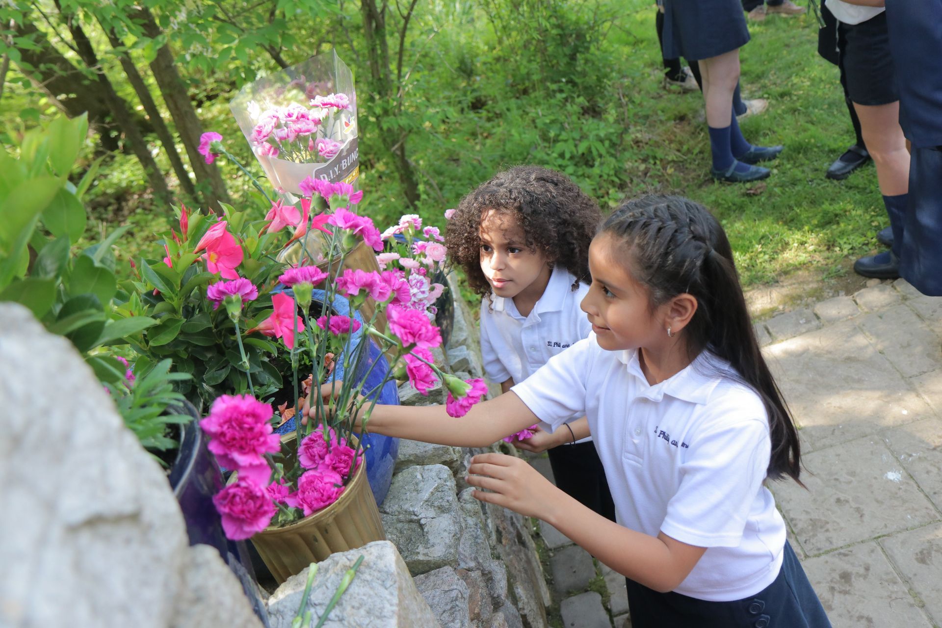 Two young girls are looking at flowers in a garden.