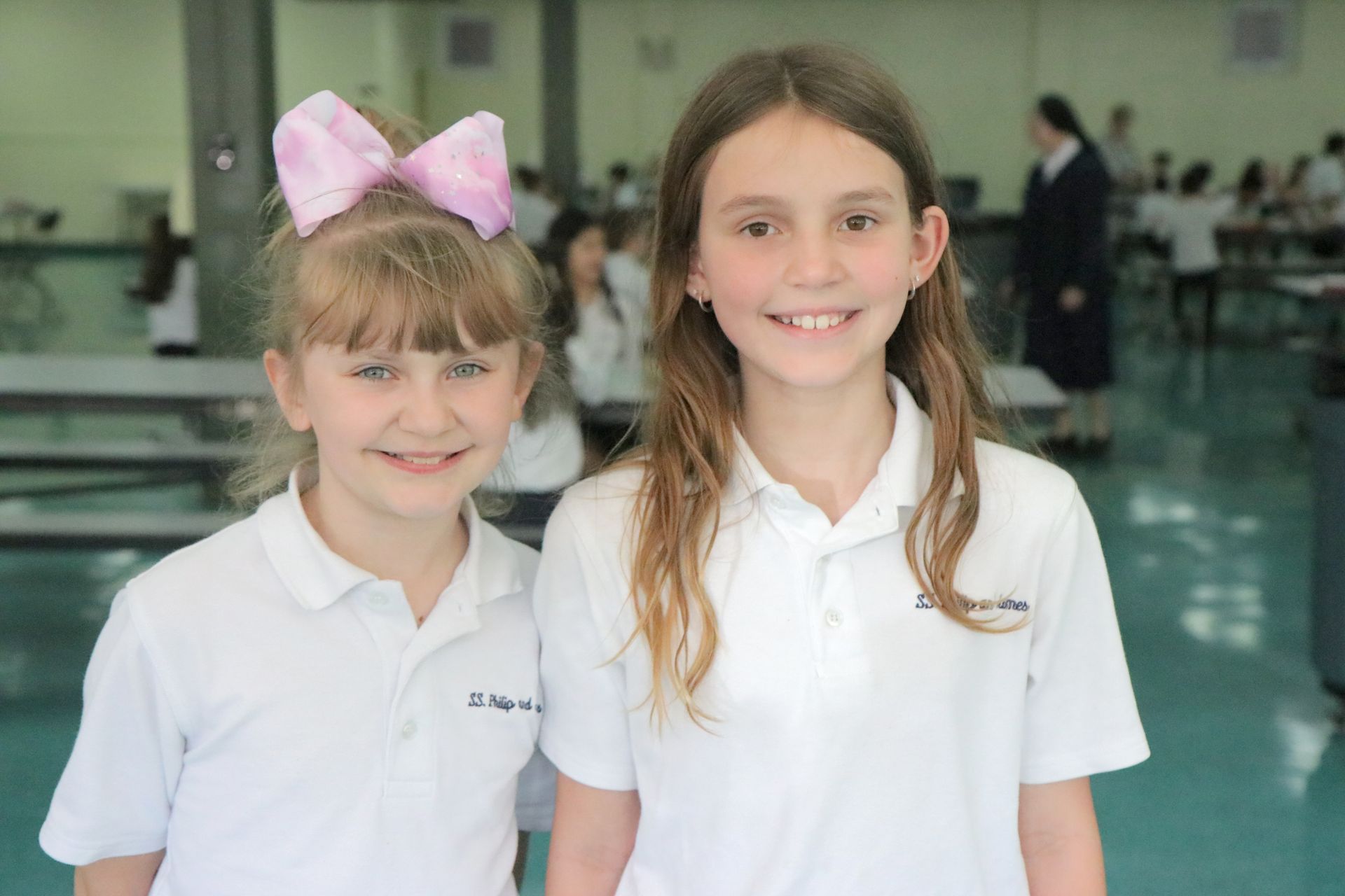 Two young girls are posing for a picture in a school cafeteria.