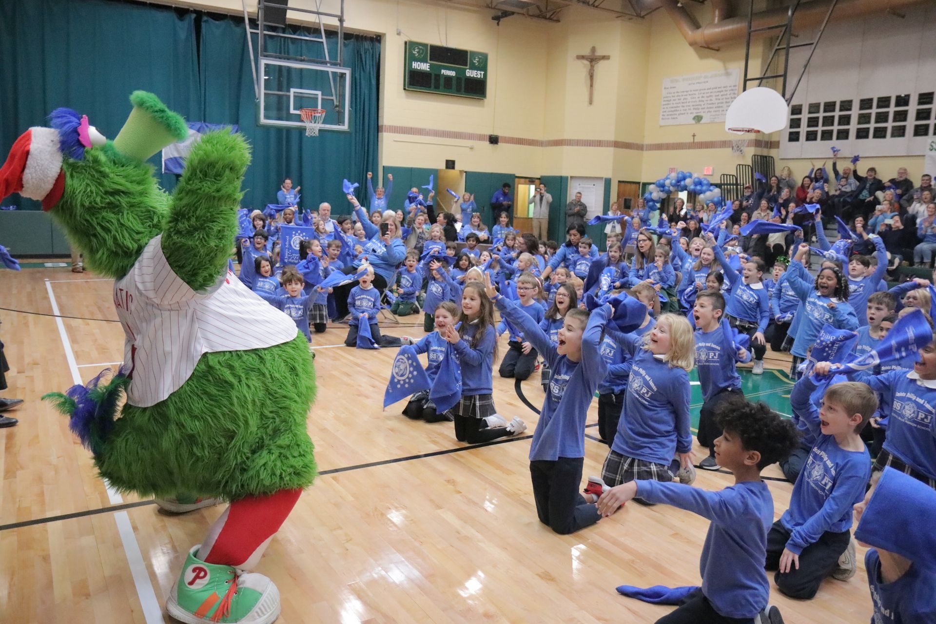 A mascot is standing in front of a crowd of children in a gym.