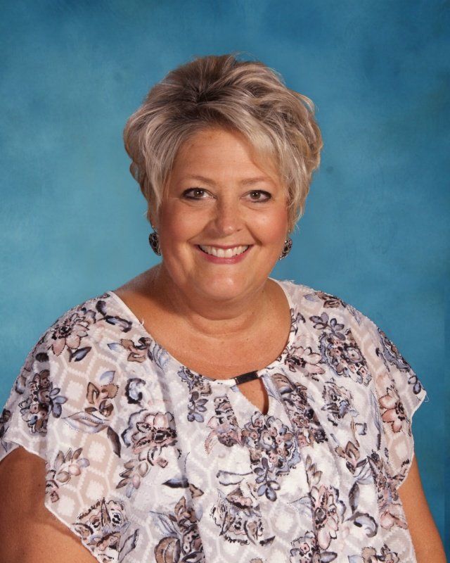 A woman in a floral shirt is smiling in front of a blue background.