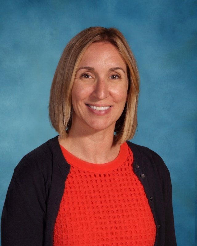 A woman wearing a red sweater and a black cardigan is smiling for the camera.