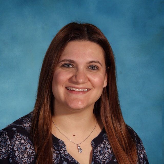 A woman wearing a necklace and a blue shirt smiles for the camera