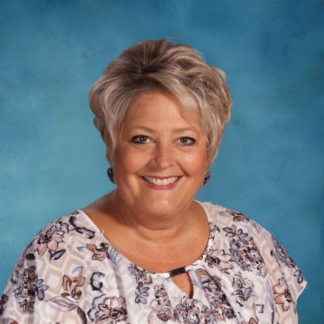 A woman in a floral shirt is smiling in front of a blue background