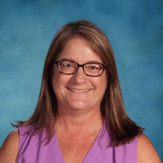 A woman wearing glasses and a purple shirt smiles for the camera