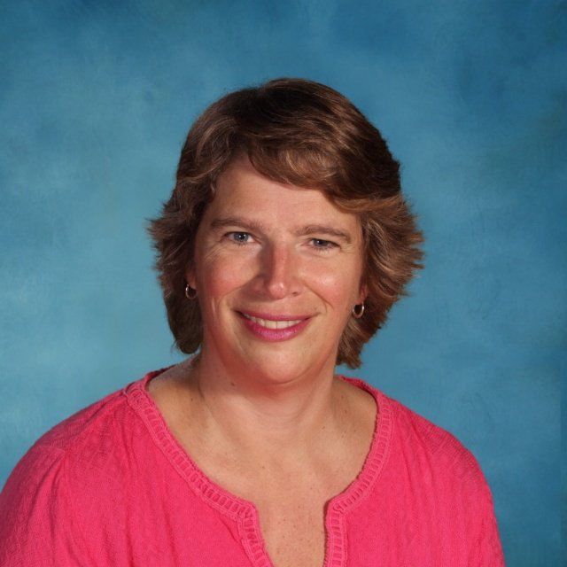 A woman in a pink shirt is smiling in front of a blue background.