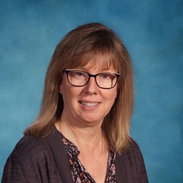 A woman wearing glasses is smiling in front of a blue background