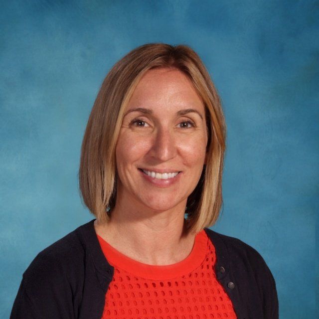 A woman wearing a red shirt and a black cardigan smiles for the camera