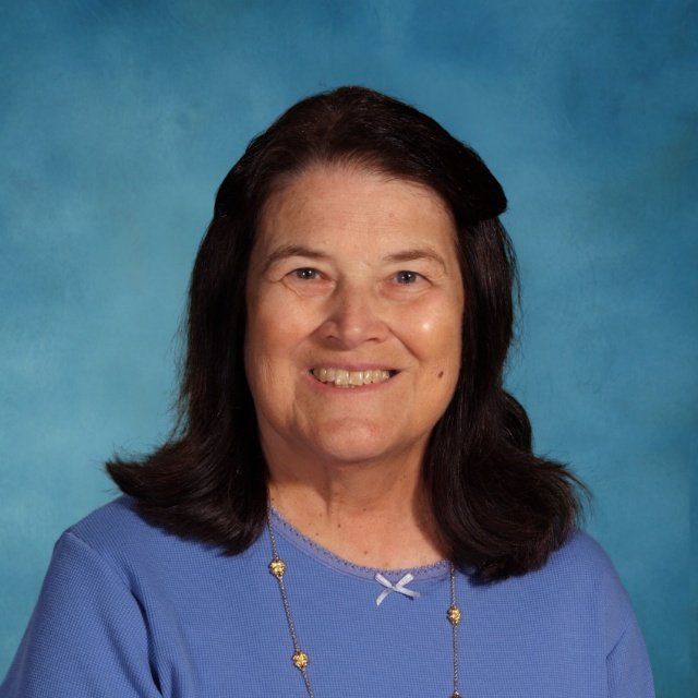 A woman in a blue shirt and necklace is smiling for the camera