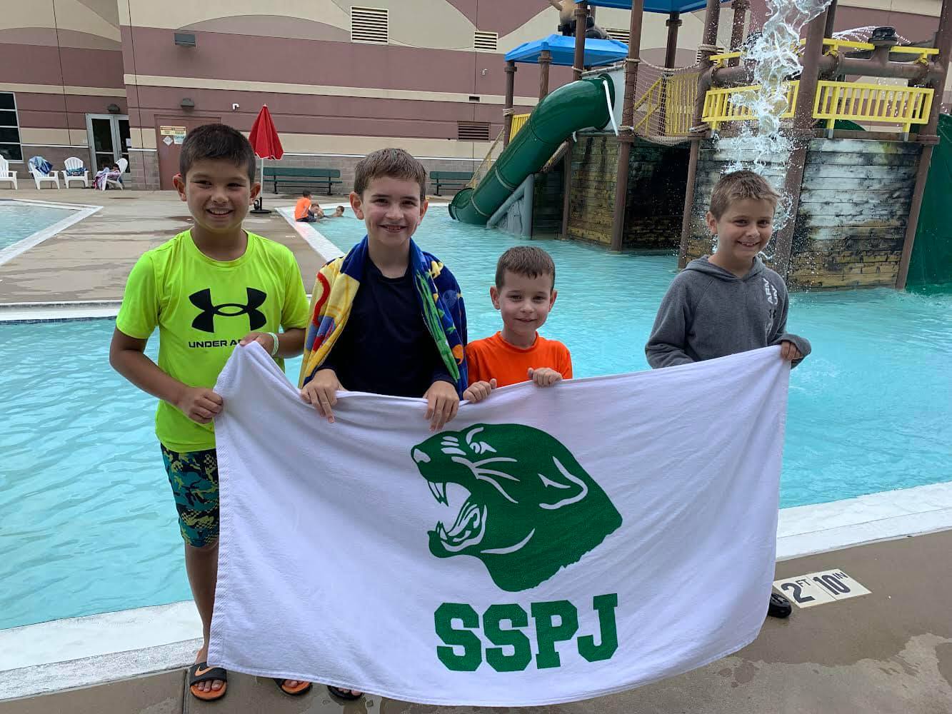 A group of young boys are standing next to a swimming pool holding a flag that says sspj.
