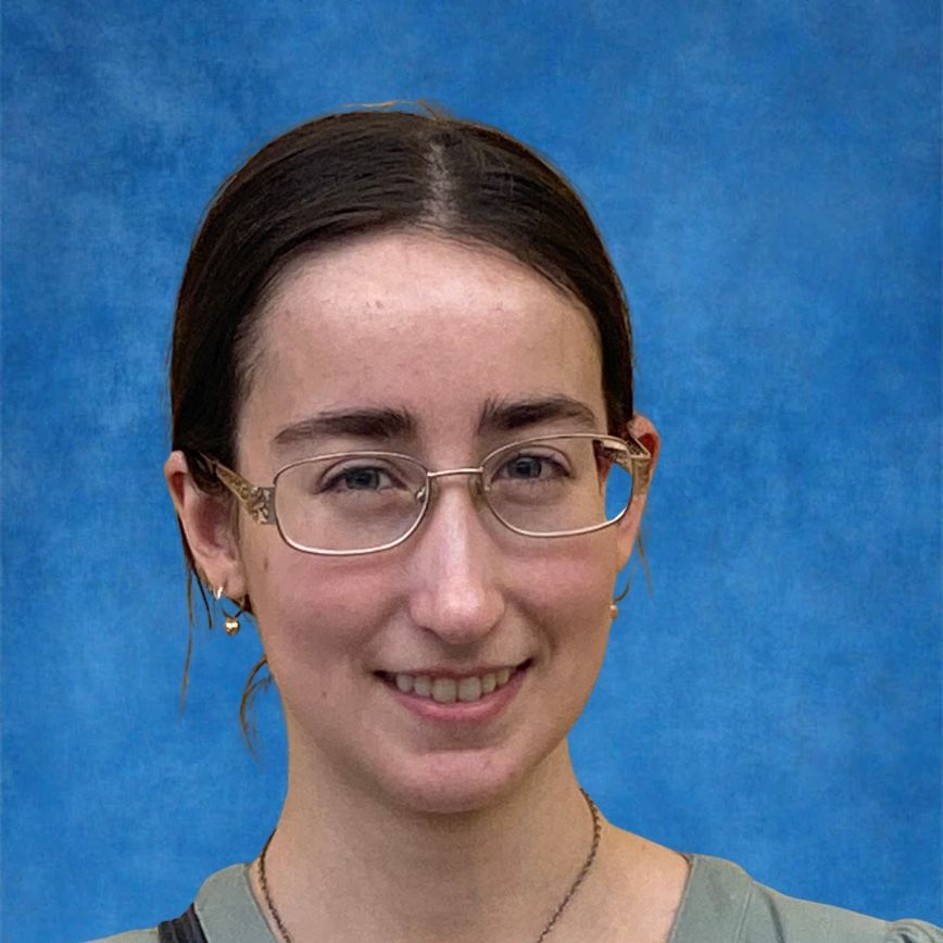 A woman is smiling for the camera while wearing a lanyard around her neck.
