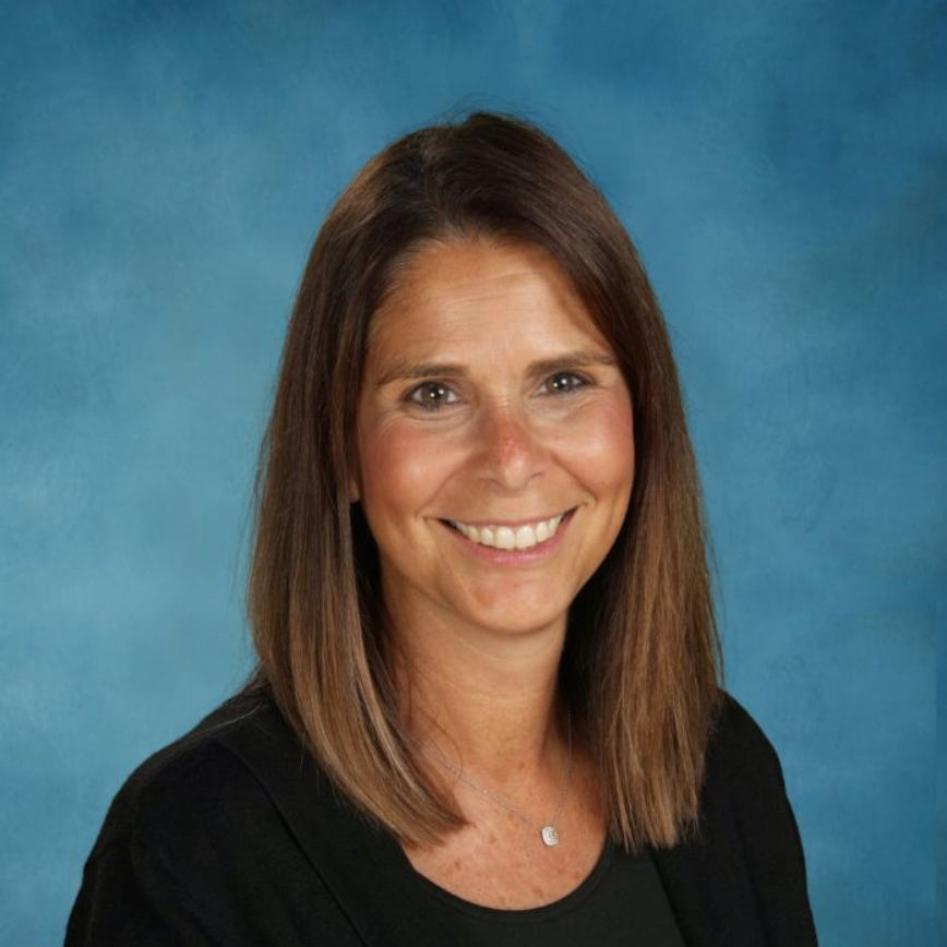 A woman wearing a necklace is smiling in front of a brick wall