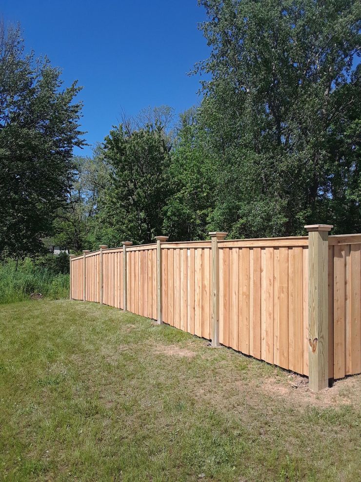 Wooden privacy fence along a grassy yard with trees under a clear blue sky