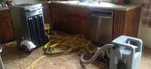 Kitchen with yellow hoses and cleaning equipment sprawled across the floor near cabinets and a dishwasher.