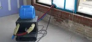 Blue backpack on a black suitcase with cables, beside a brick wall on a tiled floor.