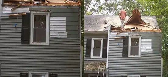 Damaged gray house with roof torn open, debris exposed near the chimney.