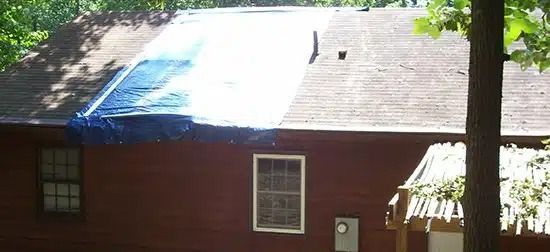 House roof with a bright blue tarp patch and trees casting shade over the exterior