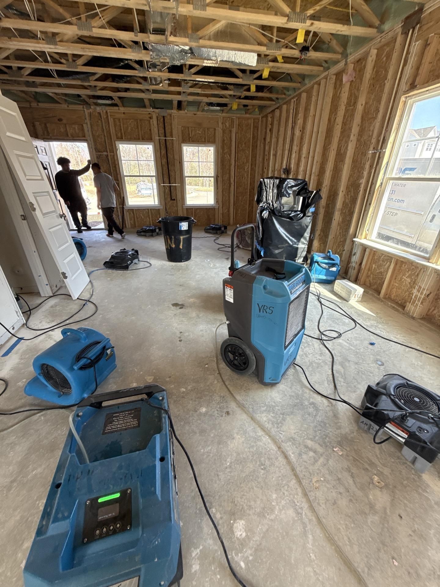 Construction site interior with exposed framing, tools, and workers near windows.