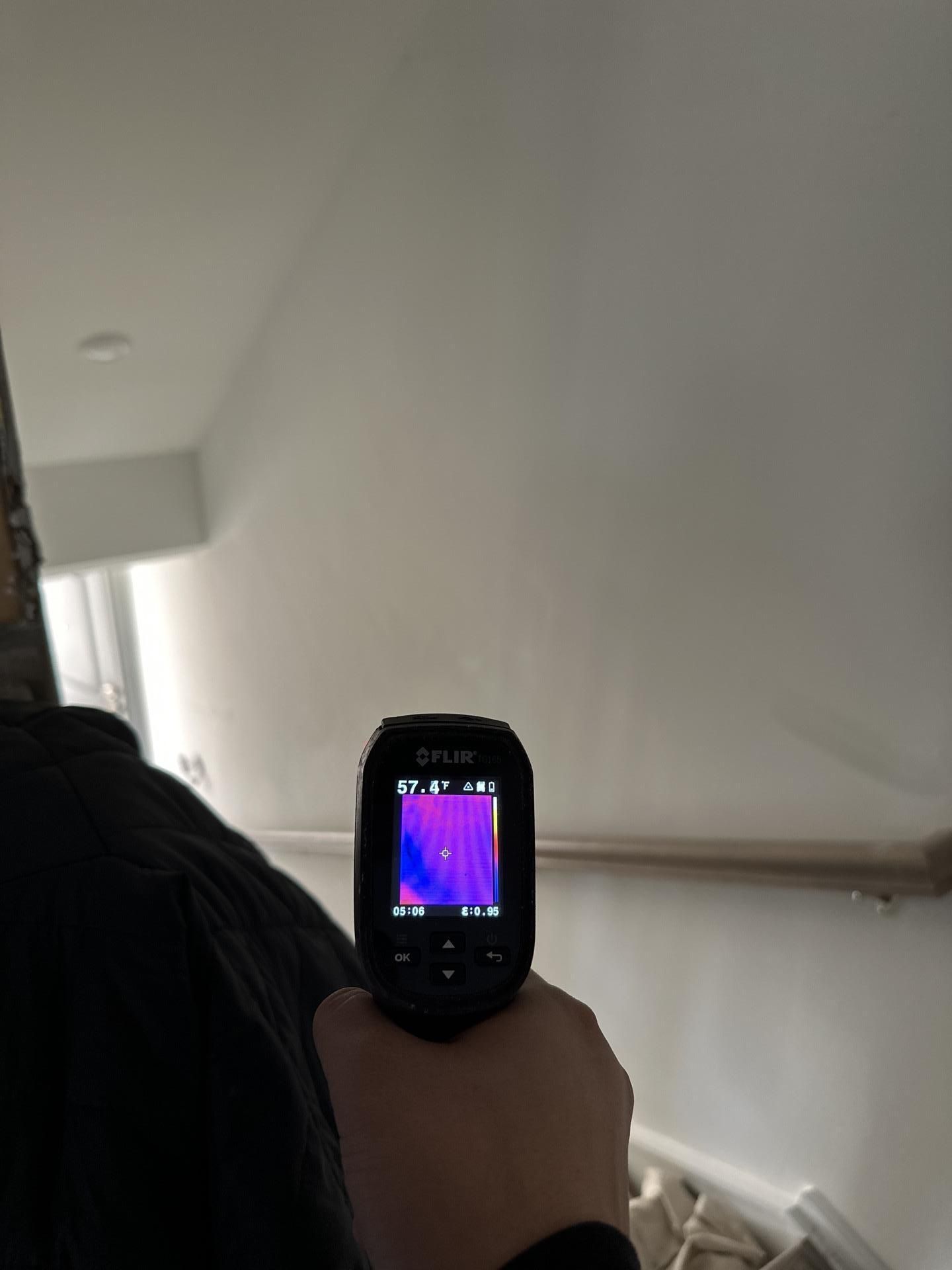 Hand holding a thermal camera showing a purple heat map in a white hallway