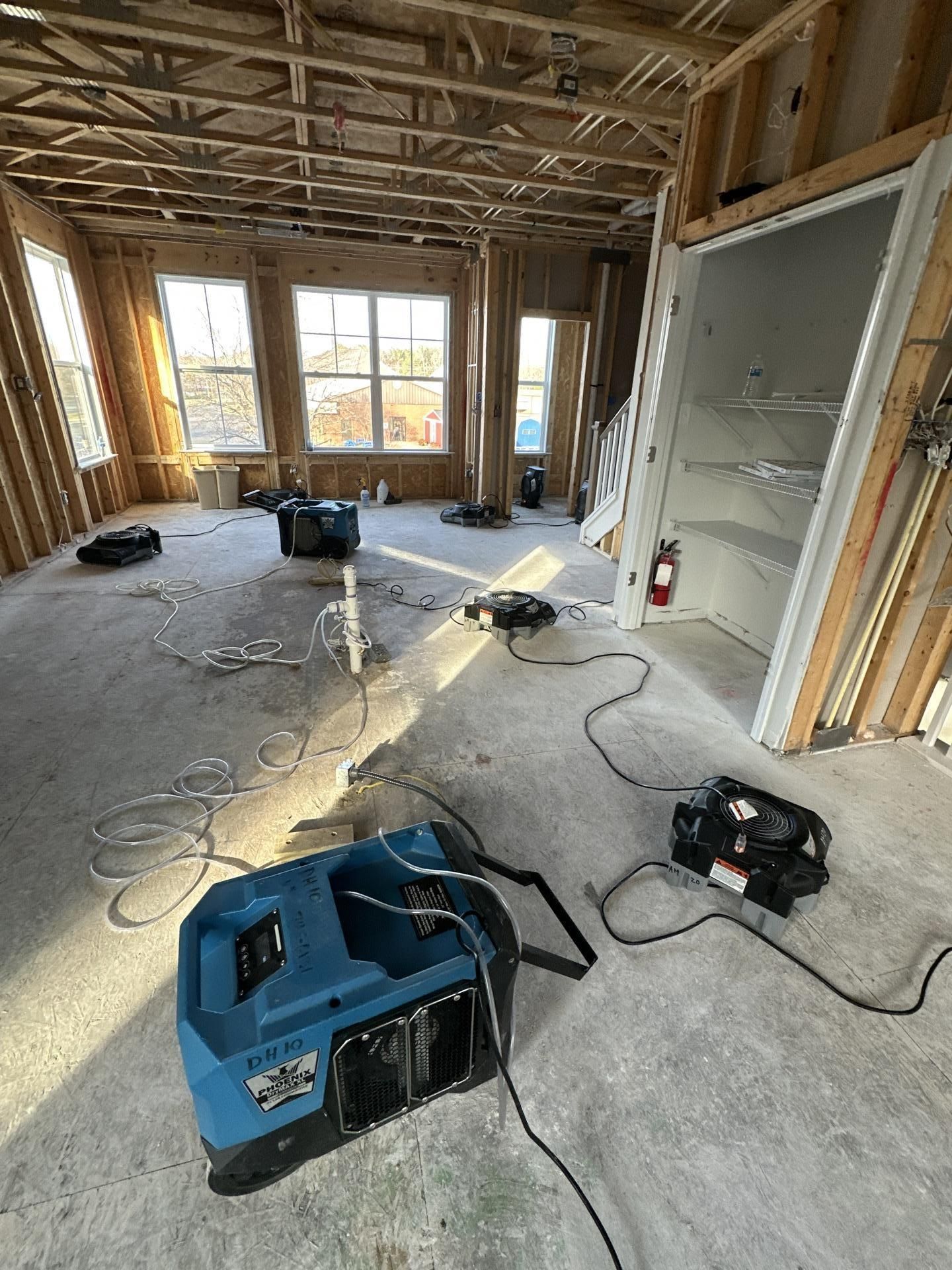 Construction room with exposed framing, tools, cords, and a blue dehumidifier on the floor.