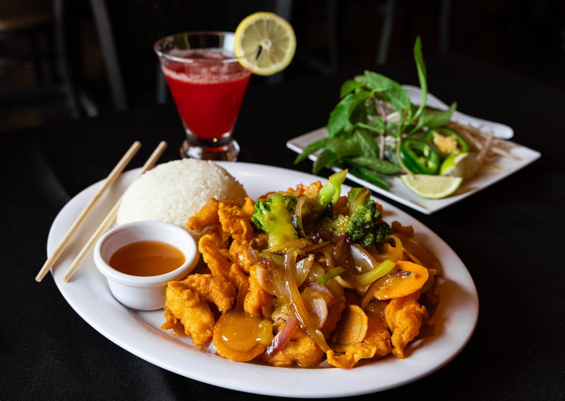 Plate of saucy fried chicken with dipping sauce, red drink, and side salad on a dark table