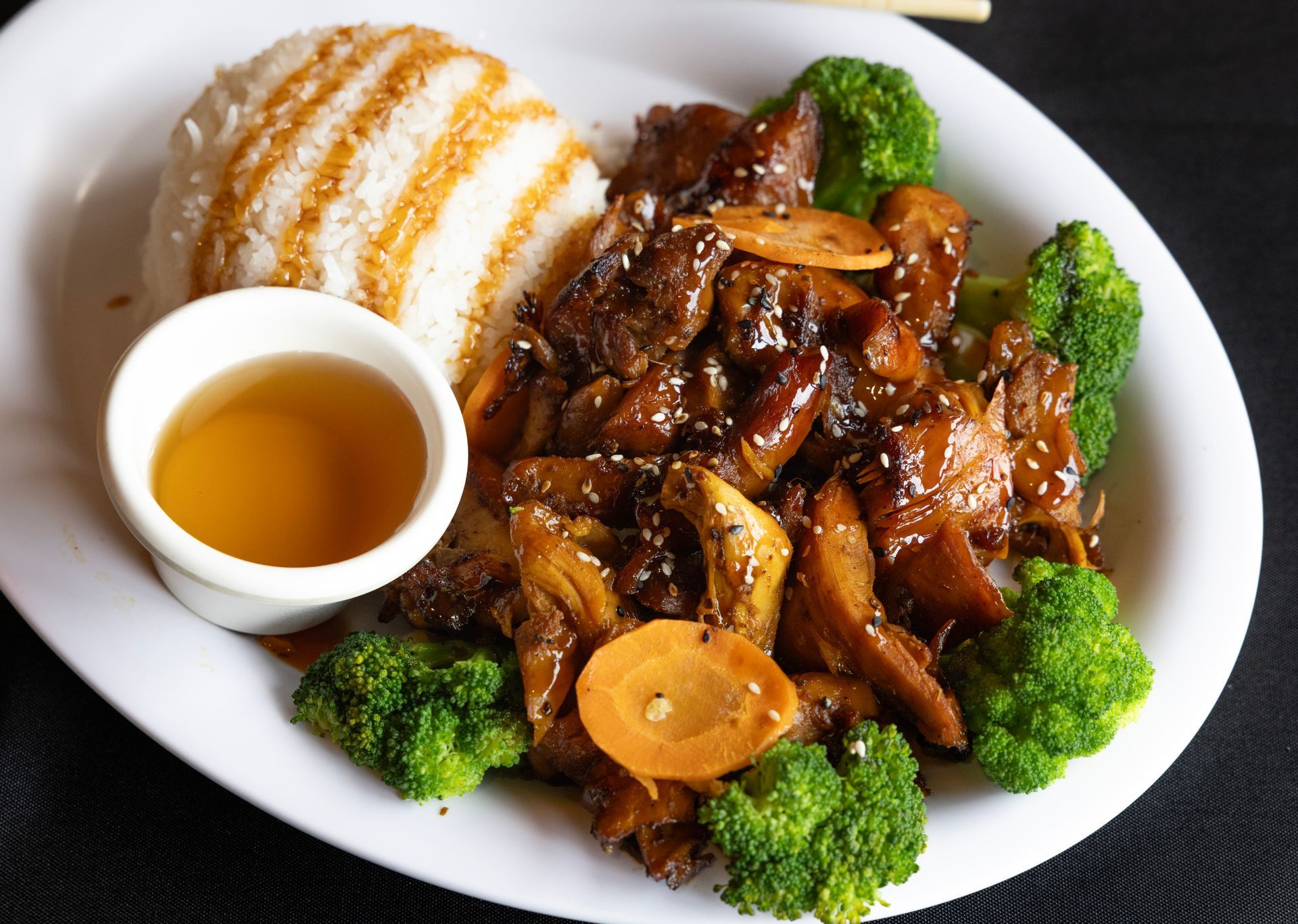 Plated stir-fry with broccoli, rice, and dipping sauce on a white plate