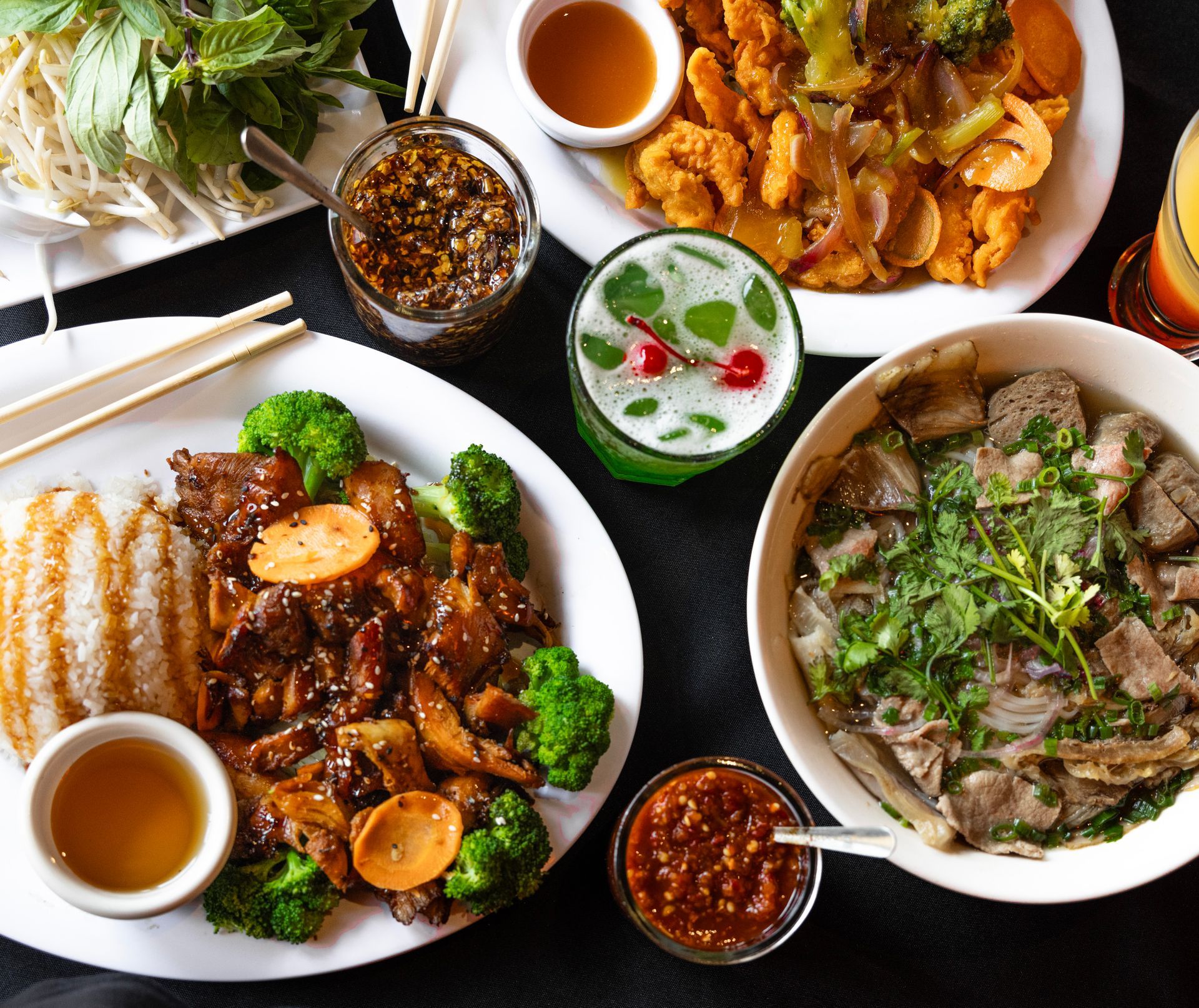 Assorted Vietnamese dishes on a table, with bowls of soup, grilled meat, herbs, and dipping sauces.