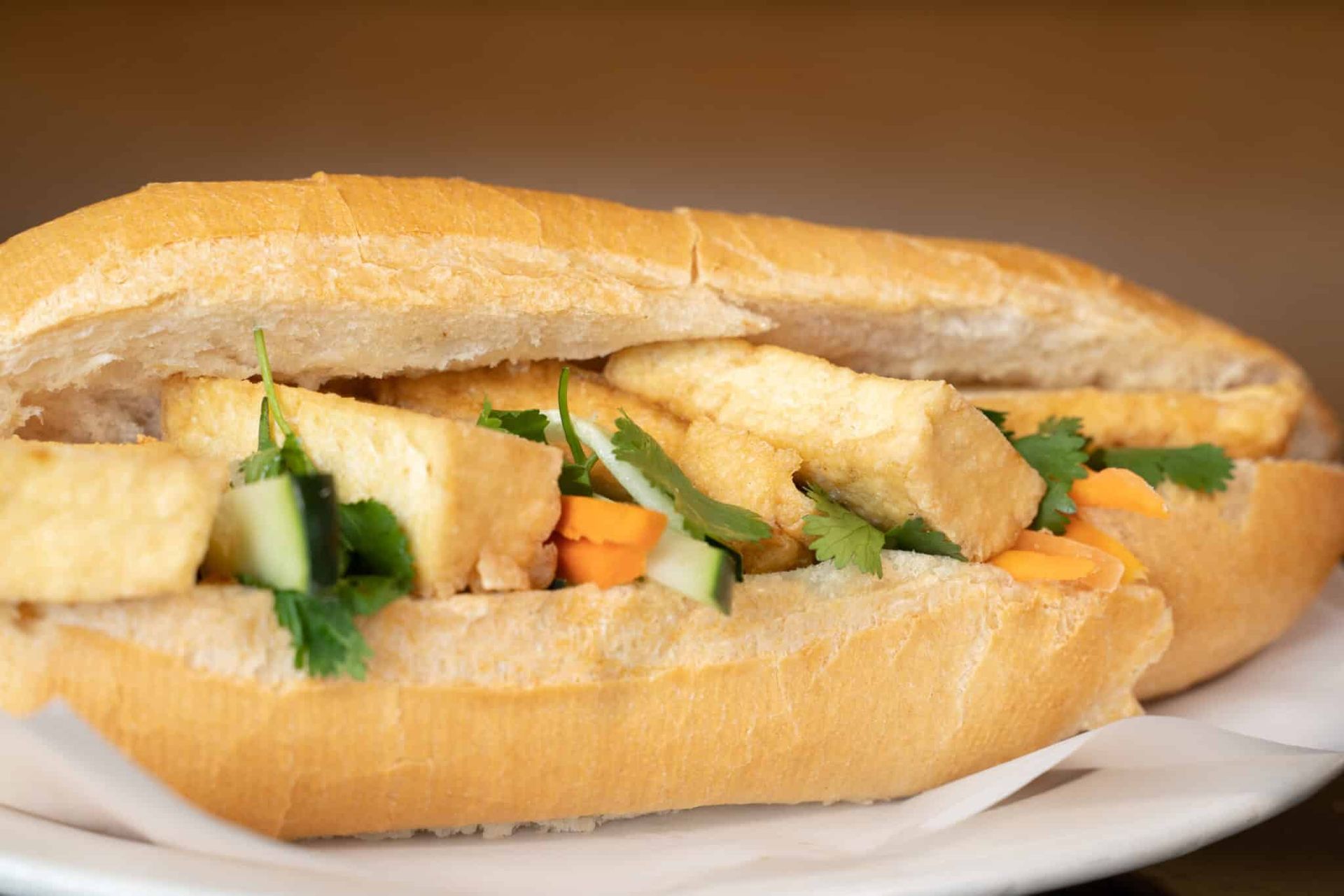 Sandwich with lettuce, cucumber, and fried filling on a white plate