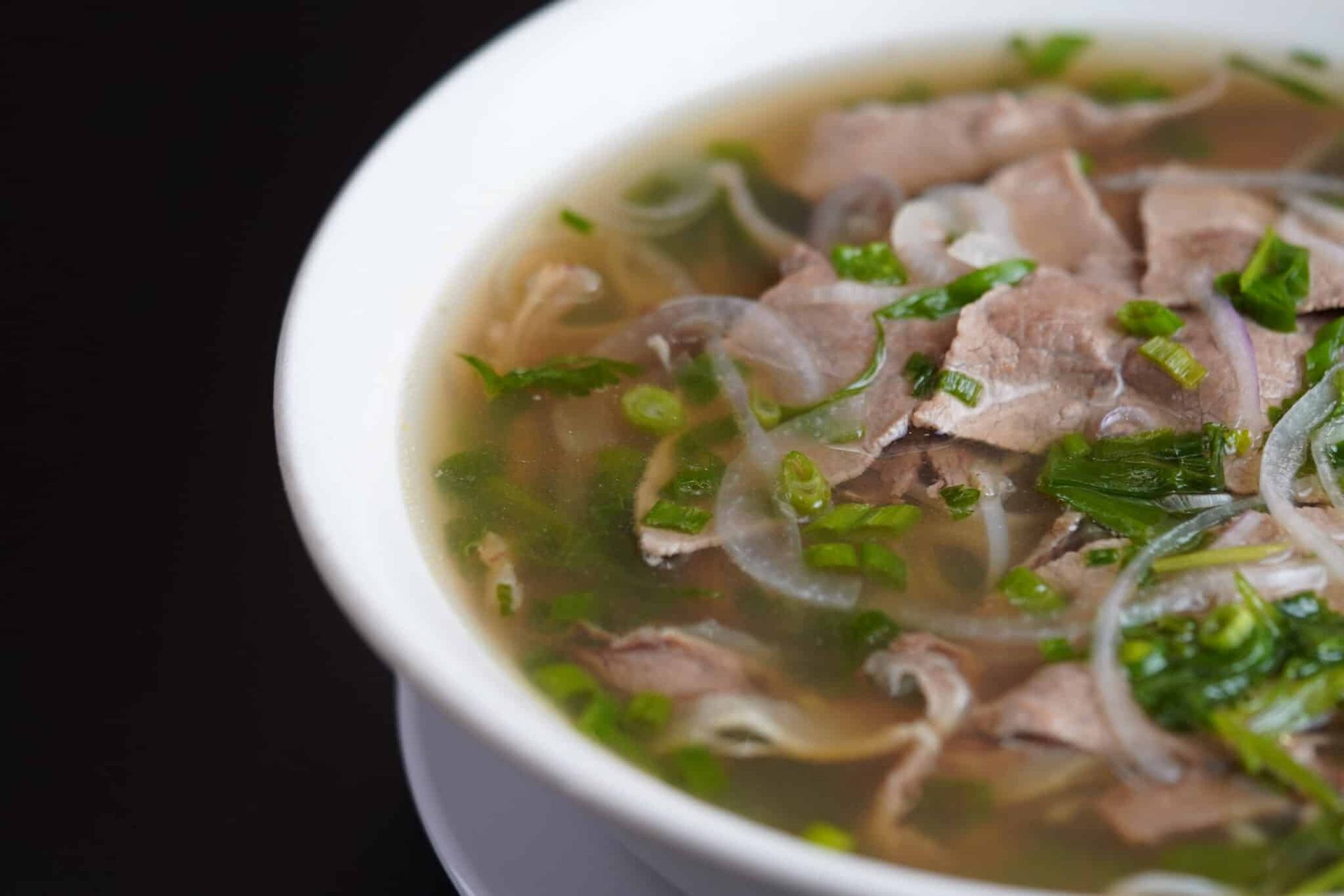 Bowl of noodle soup with sliced meat, green herbs, and clear broth